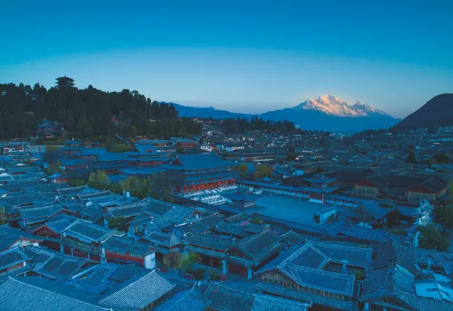 Tiled roofs of Lijiang Old Town at dusk with a snow-covered mountain in the distance