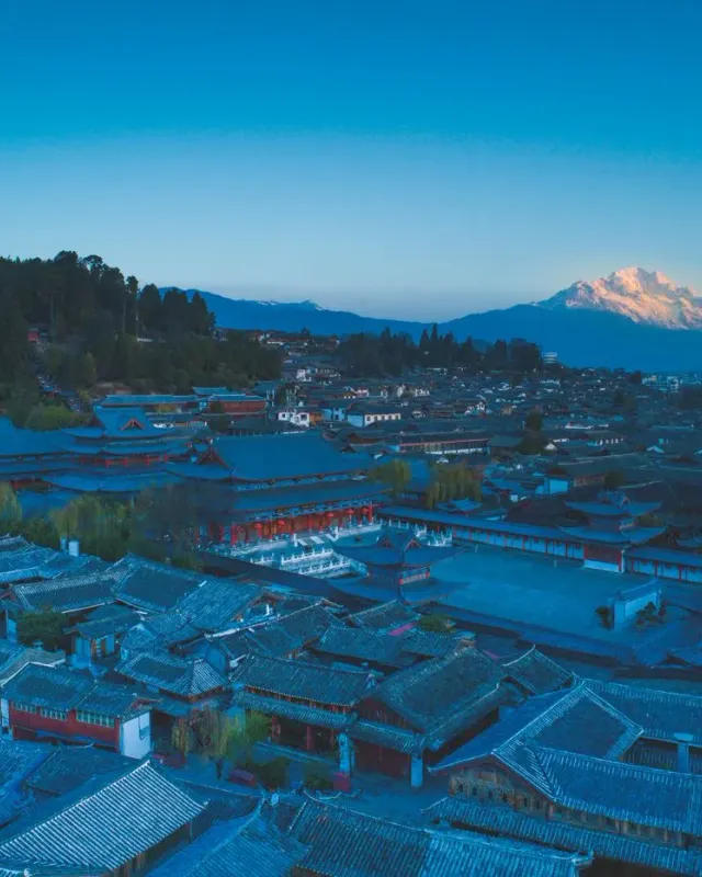 Tiled roofs of Lijiang Old Town at dusk with a snow-covered mountain in the distance
