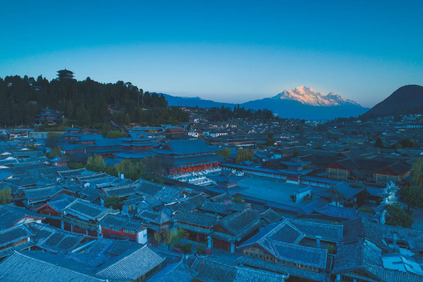 Tiled roofs of Lijiang Old Town at dusk with a snow-covered mountain in the distance