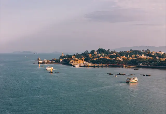 Ferries crossing the water beside the tree-covered coast and buildings of Gulangyu, Xiamen