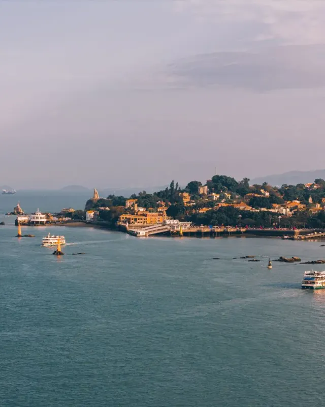 Ferries crossing the water beside the tree-covered coast and buildings of Gulangyu, Xiamen