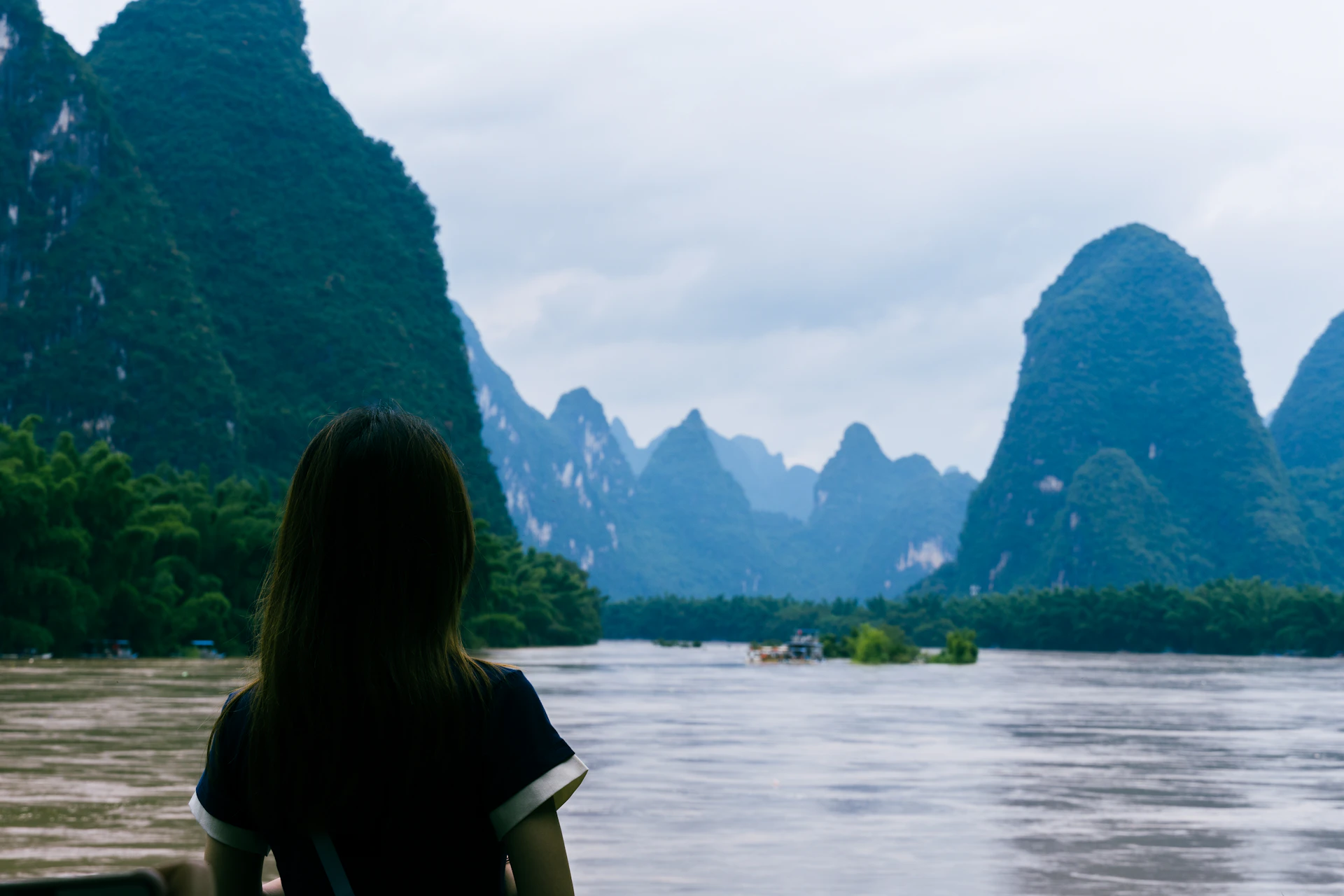 A traveller beside the Li River and limestone peaks in Yangshuo, Guilin, Guangxi
